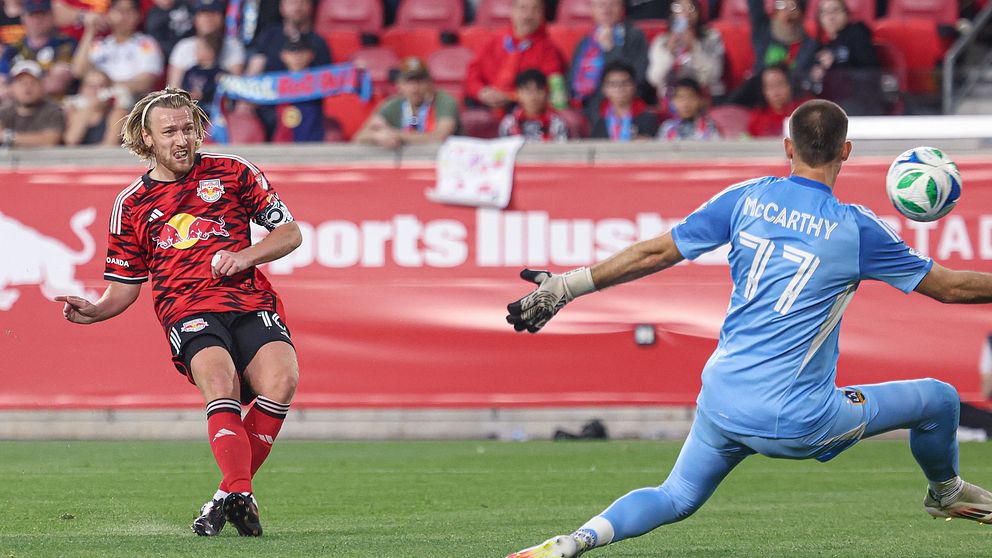 Fotbollsspelare skjuter mot mål medan målvakten försöker rädda med utsträckta armar.
