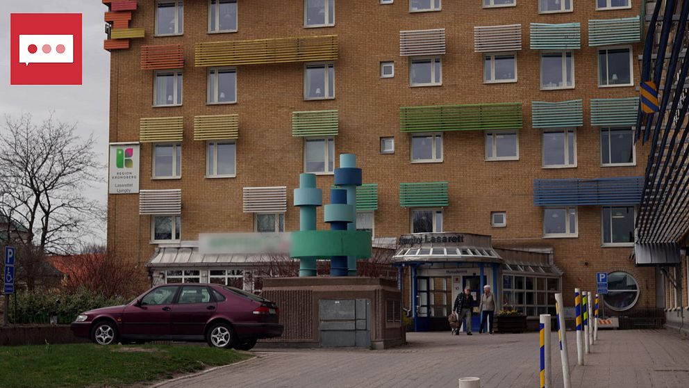 En byggnad med färgglada fönsterluckor och en modern entré. Framför entrén står en skulptur bestående av geometriska former i olika färger. Två personer går in i byggnaden medan en bil är parkerad i närheten. Träd och grönska syns i omgivningen.