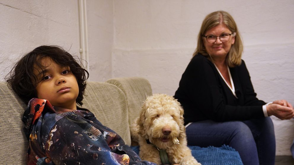 Pojke och kvinna sitter i soffa med hund