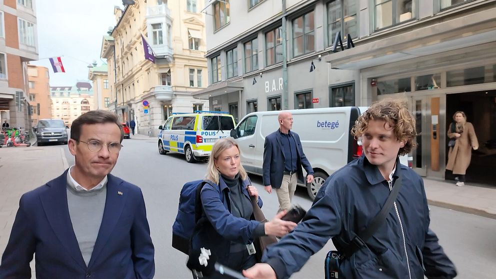 Personer promenerar på gata med polisbilar och en Infrago-skåpbil i bakgrunden.