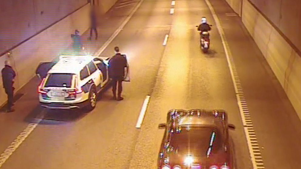 En polisbil med flera poliser närmar sig en man till fots i en biltunnel.