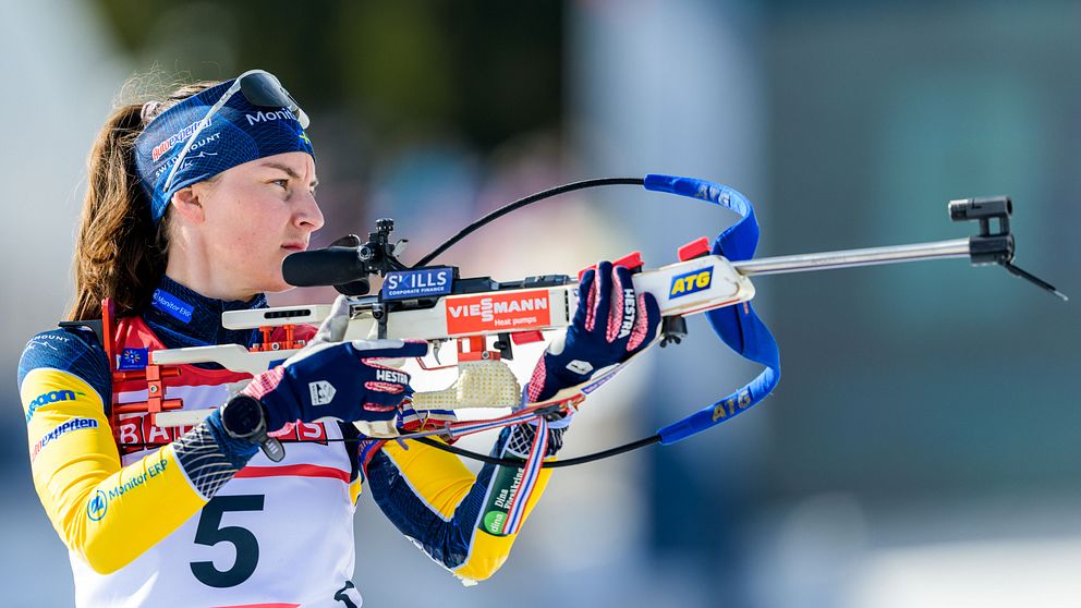 Skidskytt med gevär, tävlar i nummerlapp 5, fokuserar inför skott.
