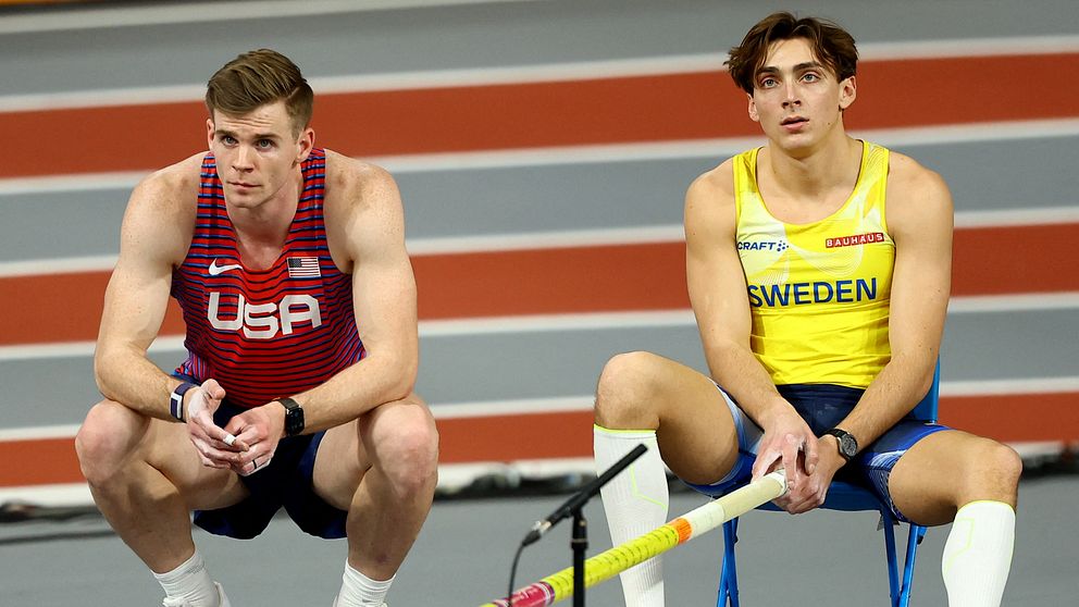Två atletiska stavhoppare, Chris Nilsen och Armand Duplantis, sitter avspända på golvet inför en tävling.