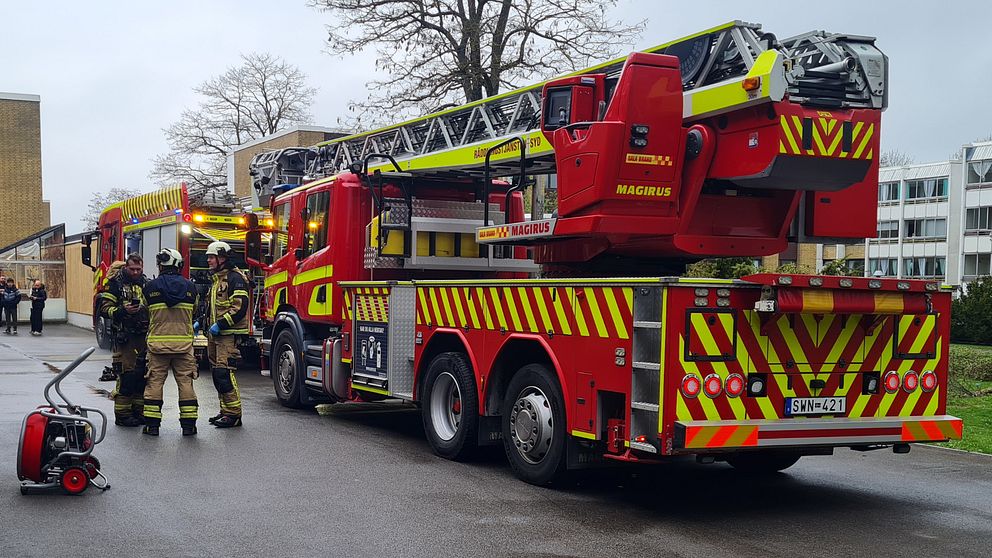 Brandbil med uppfälld stege och brandmän på väg vid höghusområde.