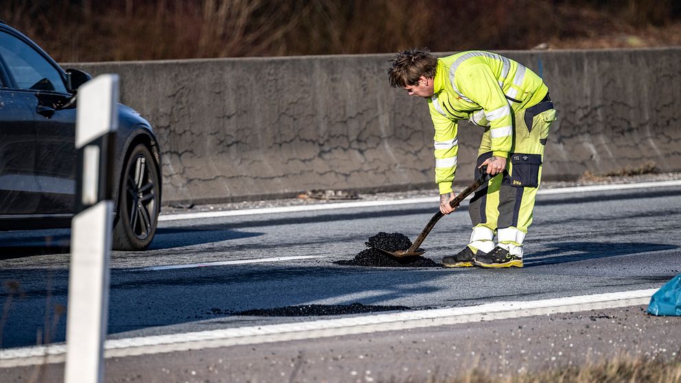 En man i  varselkläder fyller igen en vägskada på en väg.