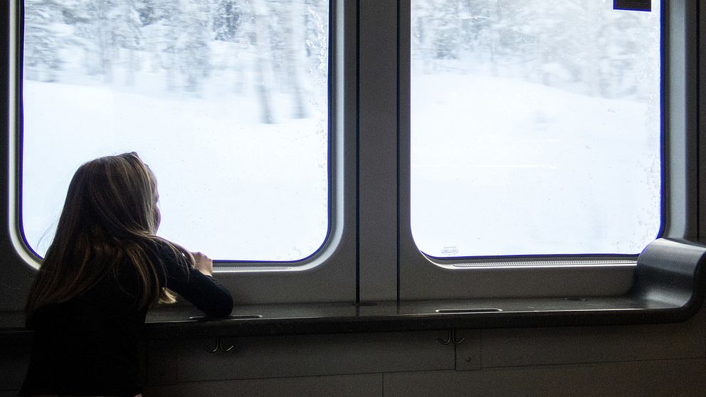 Flicka sitter på ett tåg och ser ut över ett snölandskap