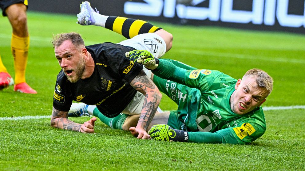 Fotbollsspelare och målvakt kolliderar och faller till marken under en match på gräsplan.