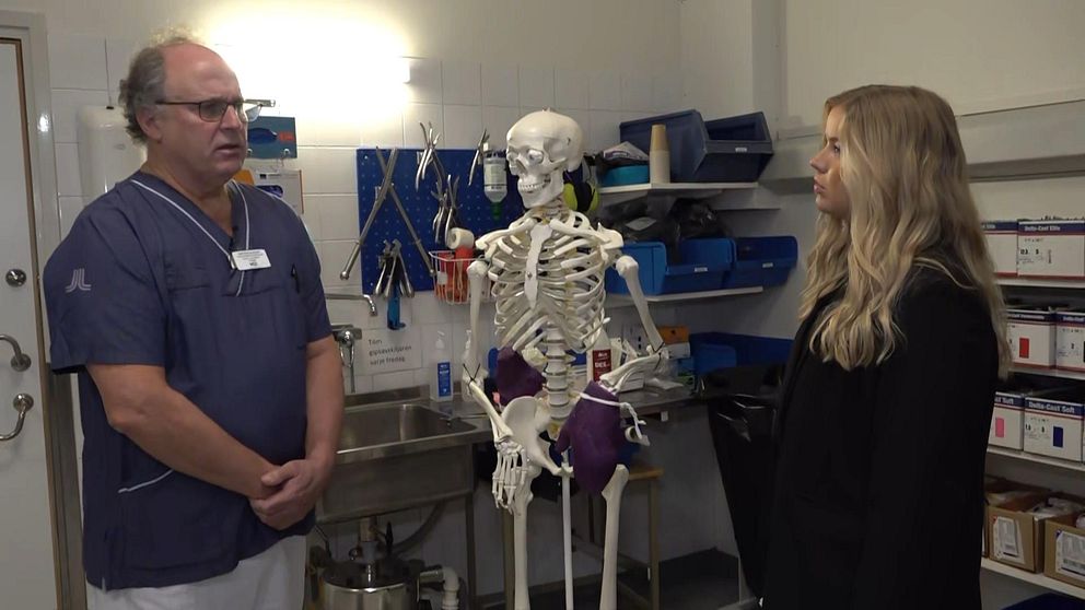 läkare med blå skjorta och ett skelett med bandage. en kvinnlig reporter frågar läkaren om skador.