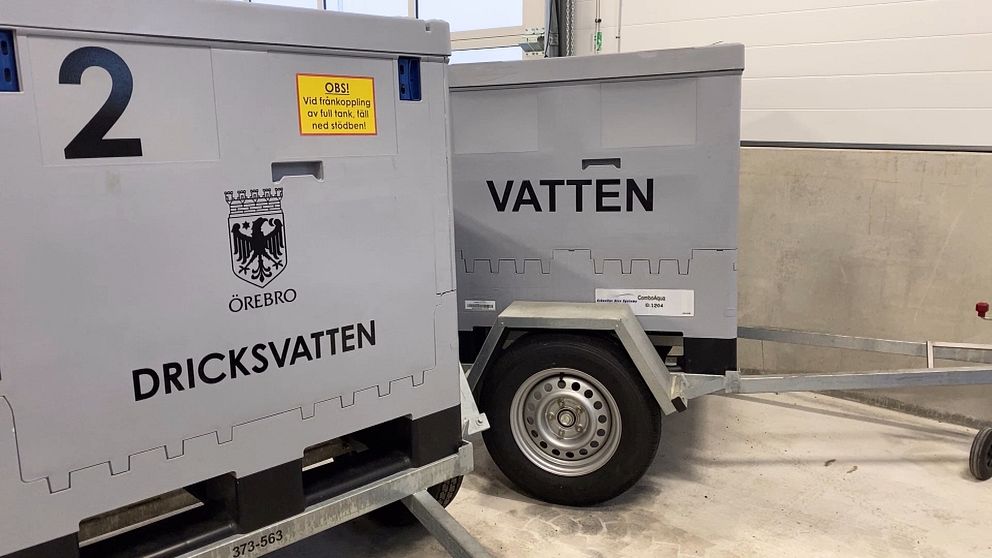 Två stora behållare märkt ”Dricksvatten” och ”Vatten” från Örebro, placerade på släpvagnar inuti en byggnad. En gul skylt varnar för att behållarna endast får hanteras med godkänd utbildning.