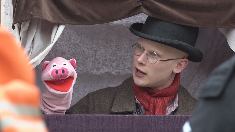 Skådespelaren Gustav Gärling sticker upp på den lilla teaterscenen för kasperdockor. Bredvid sig har han en docka av en gris som är en av karaktärerna i sagan.