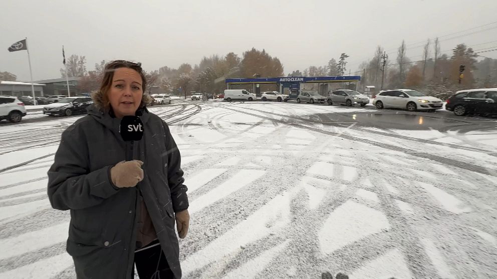 kvinna ute med mikrofon i handen framför bilar i kö