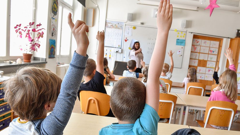 Elever i klassrum räcker upp handen.