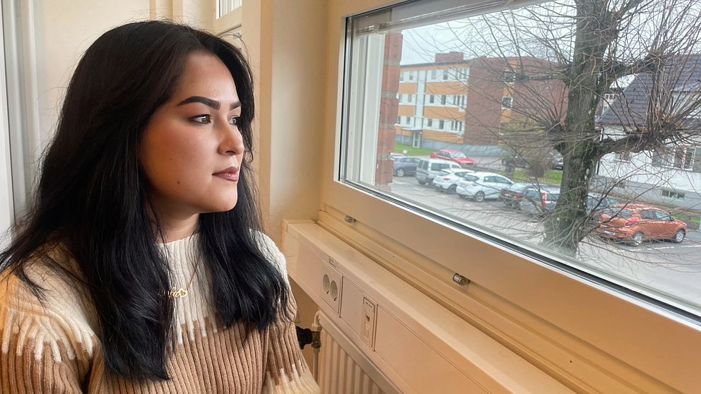 En kvinna med långt mörkt hår som tittar ut genom ett fönster