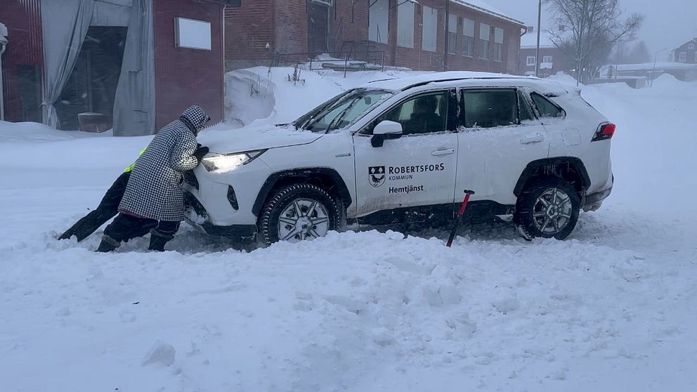 Två personer försöker få loss en bil från en snöhög.