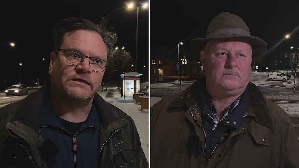 Mörk bild från en nattlig stadsmiljö som visar två män stående på en trottoar. Till vänster en man klädd i en mörk jacka, till höger en man som bär en hatt och en ljusare jacka. Båda männen ser åt olika håll mot omgivningen, med gatubelysning och en busshållplats i bakgrunden.