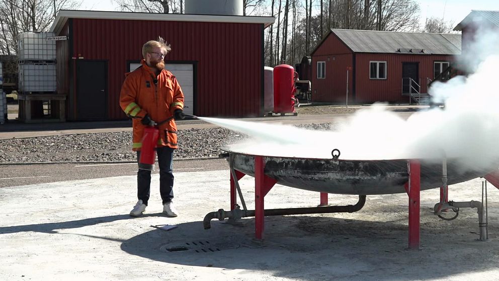 En man iförd skyddskläder sprutar med en brandsläckare på en eld vid räddningstjänstens testplats i Karlstad.