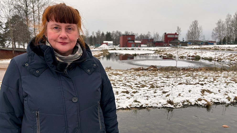 En kvinna i vinterjacka står vid några mindre vattendammar utanför ett reningsverk.