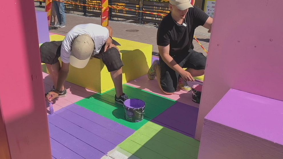 Två ungs killar som målar kvadrater och kuber på stan. De målar med rosa, lila, grön och gul färg.