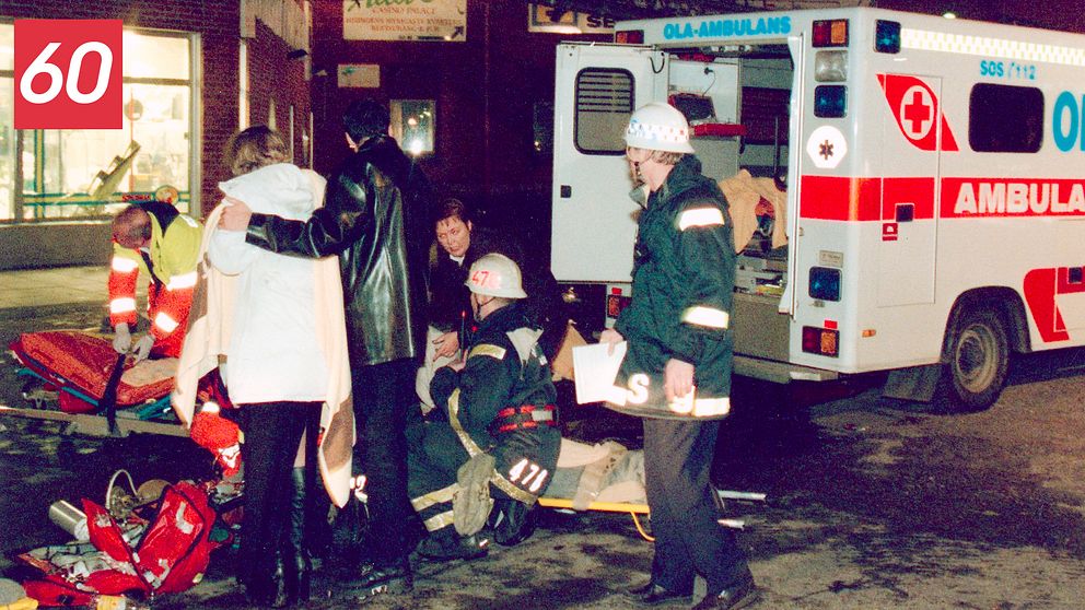 Arkivbild från 1998 efter branden på Backaplan, Hisingen, Göteborg. Ambulanspersonal och sörjande står intill ett ambulansfordon.