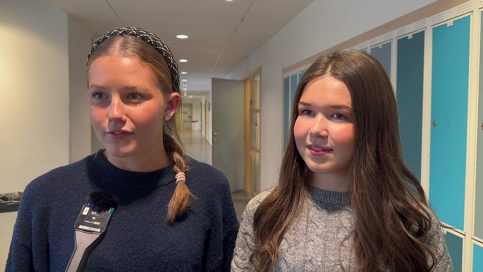 Till vänster står Filippa Swärd och till höger står Nellie Lindgren, de är elever på Sjöängsskolan i Askersund och går båda i årskurs två. De står i en korridor i skolan, men blåa skåp bakom sig.