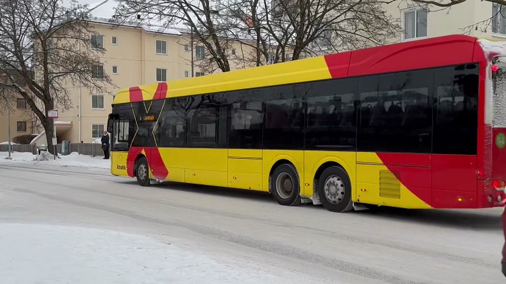 En buss som är röd och gul med ett stort X på sidan kör på en vinterväg.