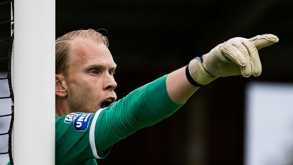 Målvakt i grönt matchställ står vid målstolpen och pekar ut mot planen.