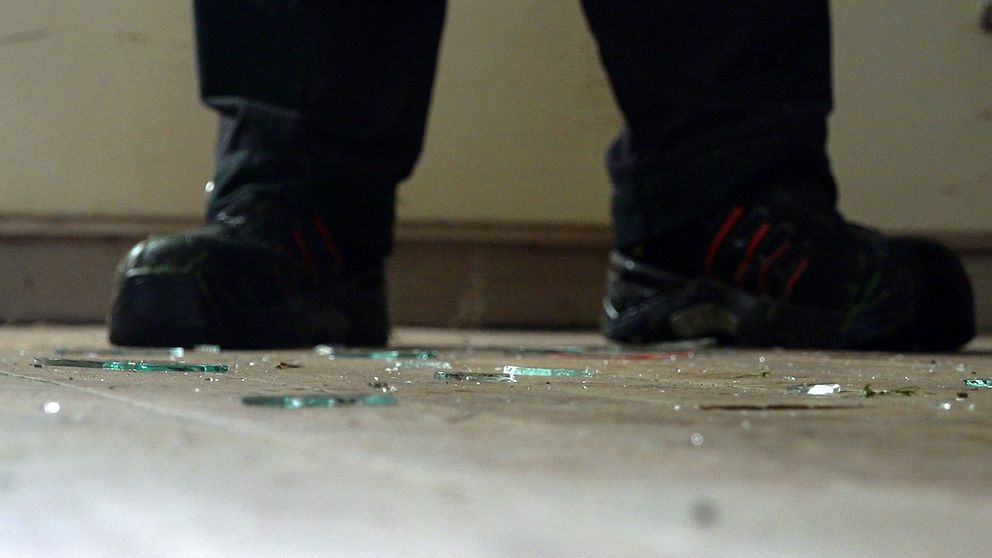 Ett par fötter med krossat glas på golvet