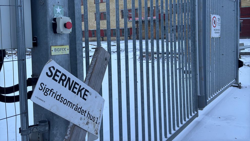 Stängd metallgrind i ett snöigt område, med en skylt som visar ”SERNEKE” och ”Sigfridsområdet hus 1”.