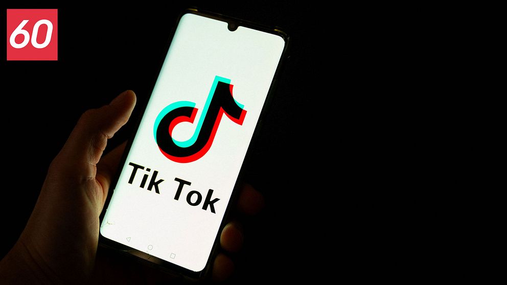 En hand som håller en mobiltelefon i mörkret där det står ”Tiktok” på mobilskärmen. En Tiktoklogga syns på skärmen.