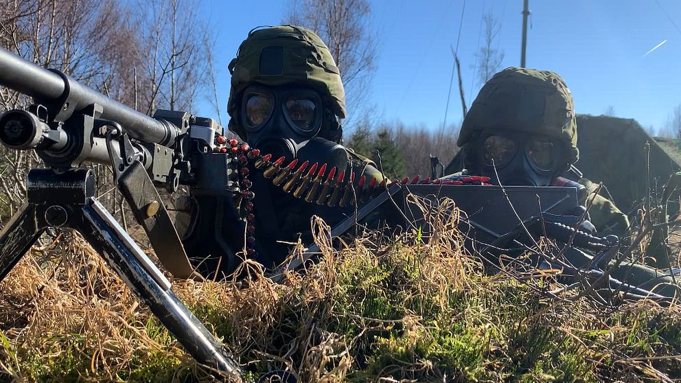 Två värnpliktiga med gasmask vid en kulspruta.