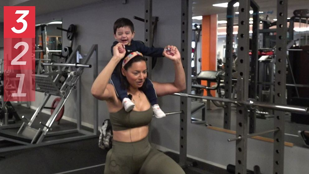 Barn sitter på mammas axlar på gymmet och de båda ser glada ut och tittar in i kameran