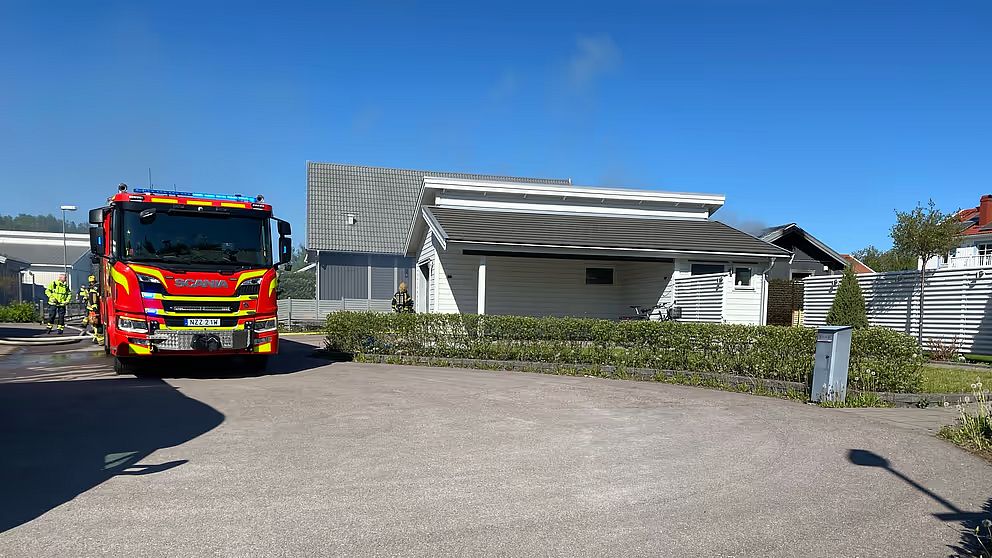 En brandbil står bredvid en grå villa vid en vändplan.