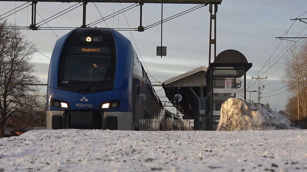 Ett blått tåg vid station, snö i förgrunden