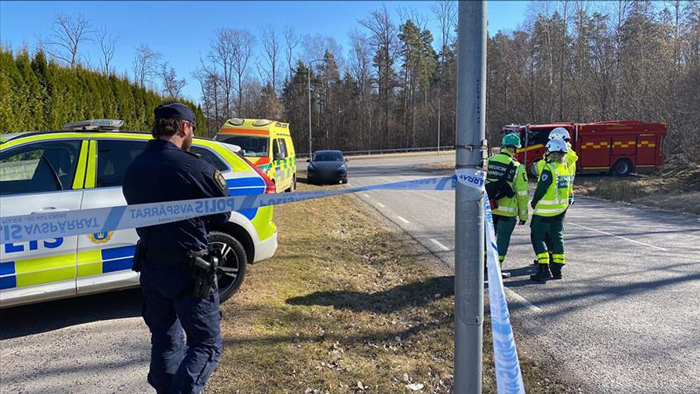 Polis och räddningspersonal vid avspärrad plats. Ambulans och brandbil synliga.