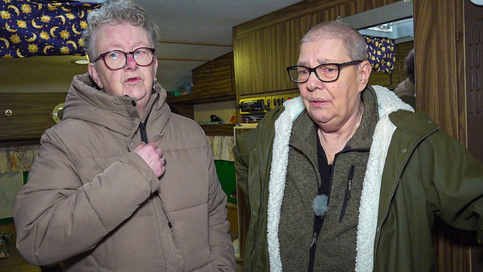 Två kvinnor med glasögon som står i en äldre husvagn. De har jackor på sig.
