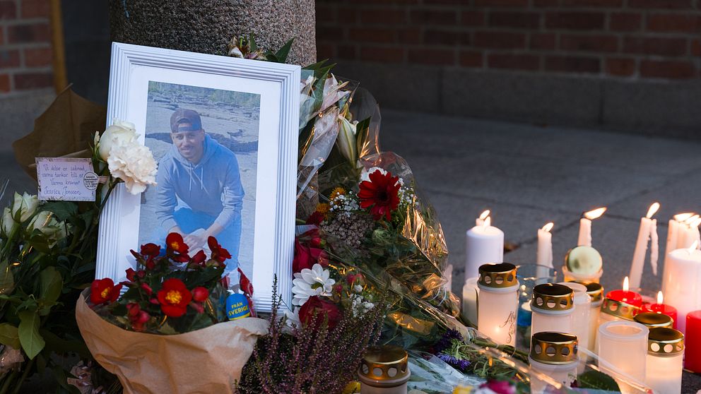 Inramad bild på 23-årig pojke, omringas av blommor och ljus på minnesplats.