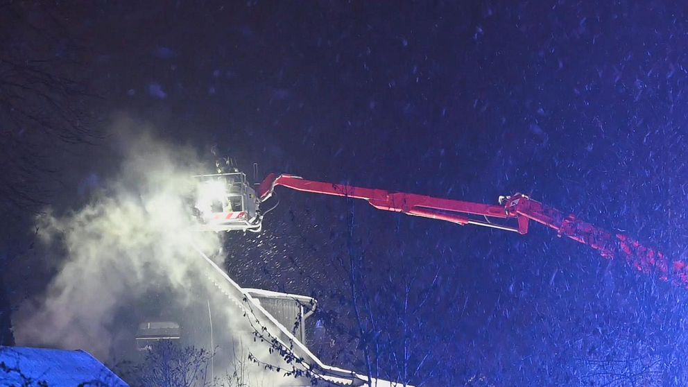Rök stiger från ett villatak och räddningstjänsten släcker från kran.
