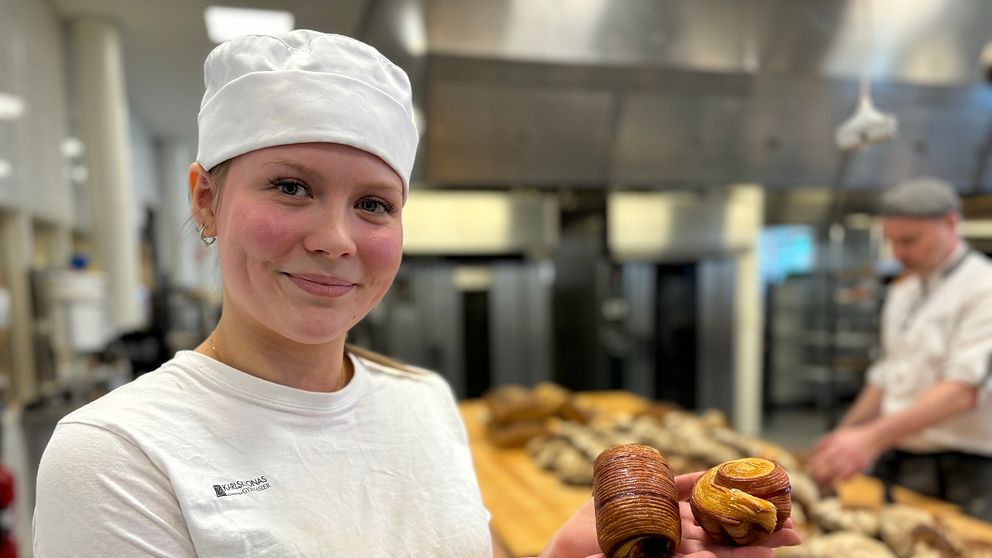 Bagare visar upp bakverk i ett bageri med bröd bakgrund.