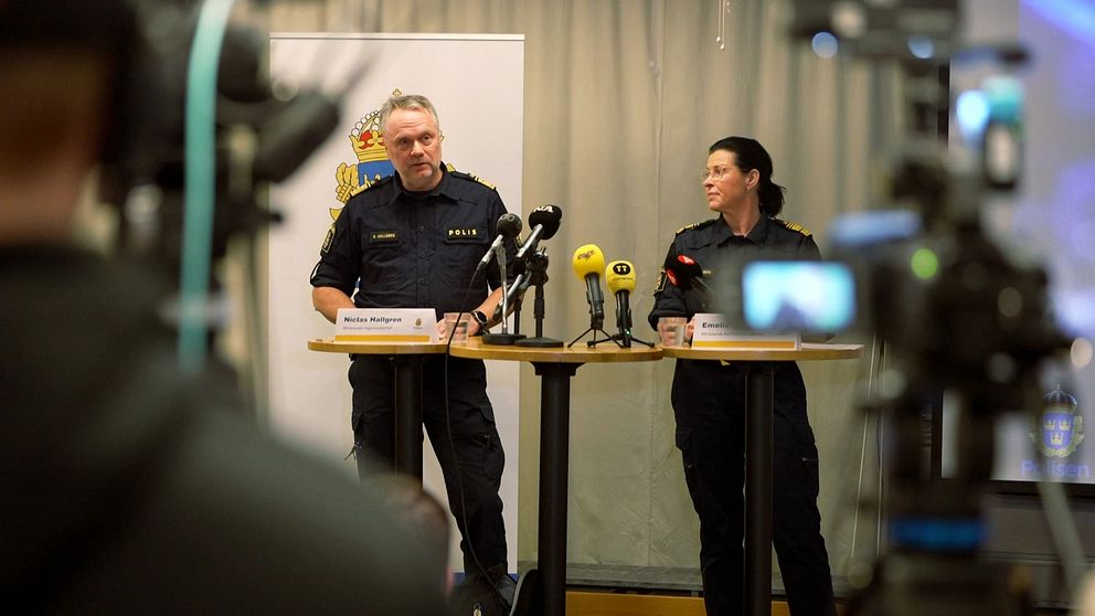 Två poliser håller presskonferens vid podium med mikrofoner.