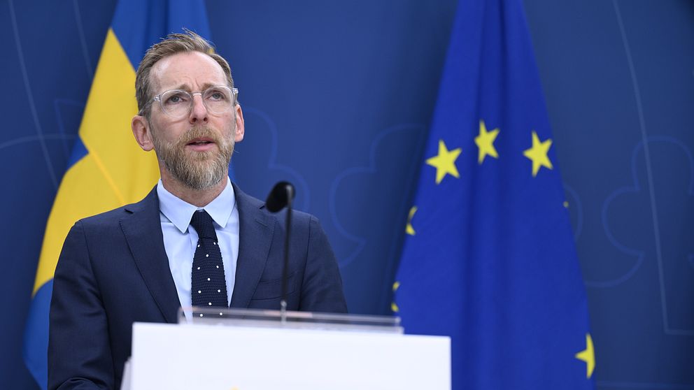 Socialminister Jakob Forssmed håller presskonferens. Bakom honom hänger svenska flaggan och EU-flaggan.