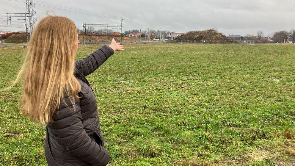 Projektledare Helena Svensson står på en äng och pekar mot en stor kulle byggt av jord