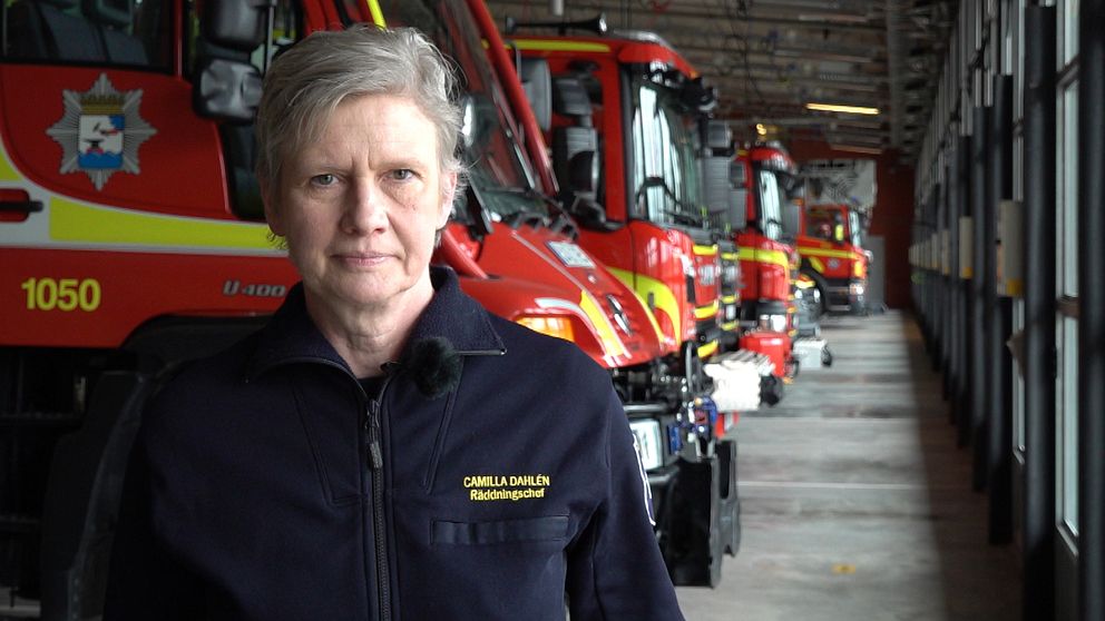 Räddningschefen står framför röda brandbilar som står uppradade i en brandstation.
