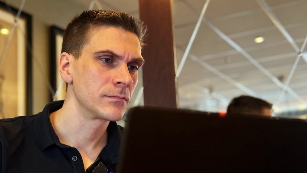 En ung man sitter på en kafé och arbetar vid en laptop, omgiven av en avslappnad atmosfär.