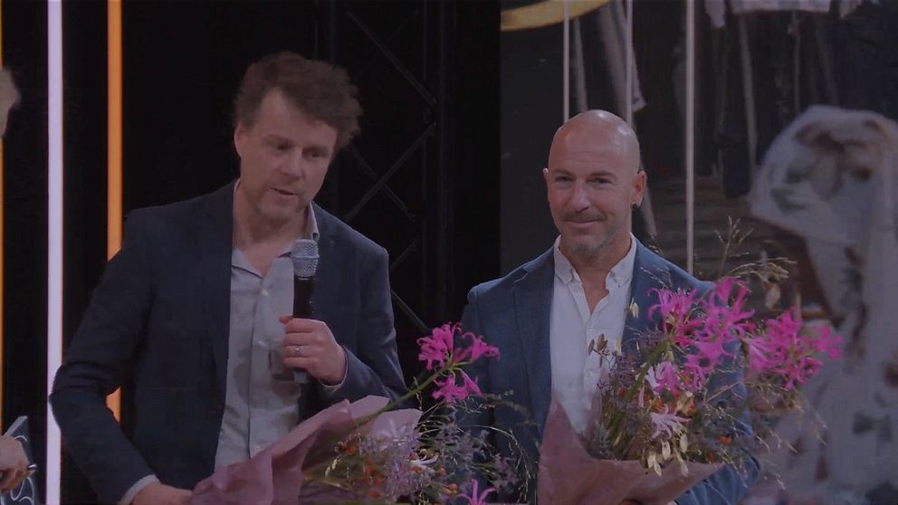 Två män står med blommor på scen