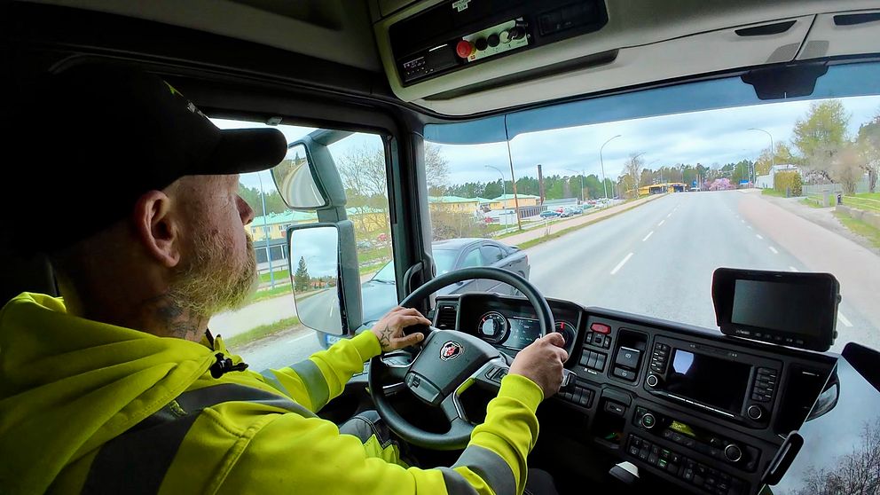 Person kör lastbil på landsväg, interiörvy av hytten.