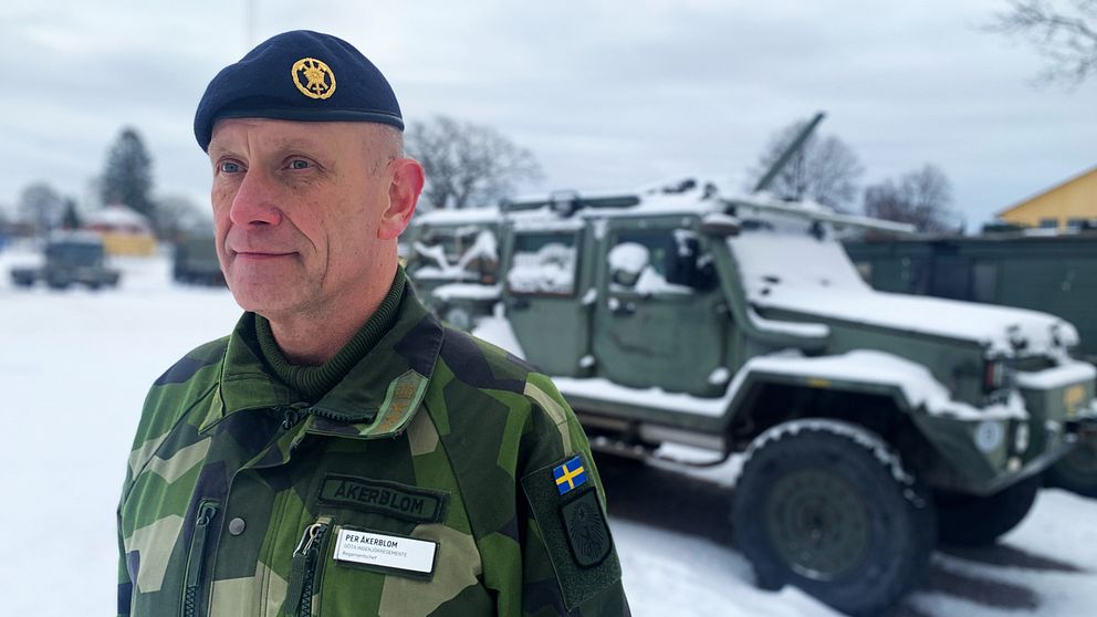 Man med blå basker och militärkläder står vid en snötäckt militärbil.