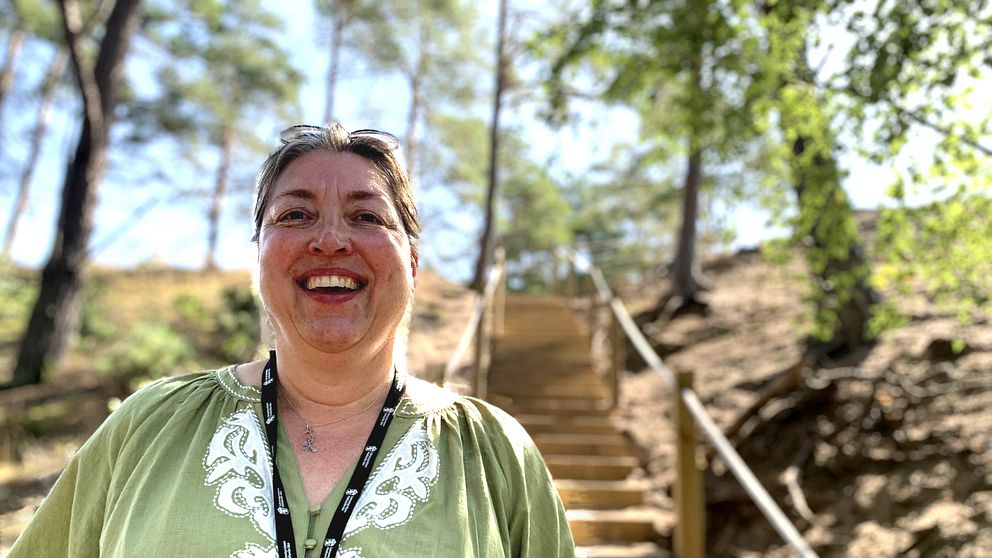Annelie Ohlsson står framför trappan som leder upp till toppen av sanddynen. Trappan är insprängd mellan träden och sanden.