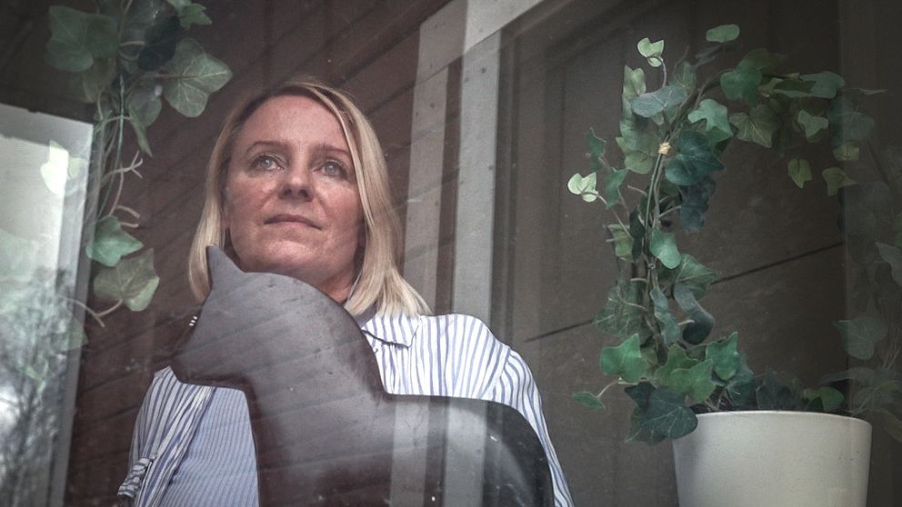 Karolin Norlén Järpeskog tittar ut genom fönstret på ett HVB-hem. Inomhusmiljö med gröna växter, en dalahäst och träpanel i bakgrunden.