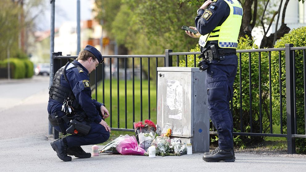 Två poliser vid en minnesplats med blommor på en trottoar.