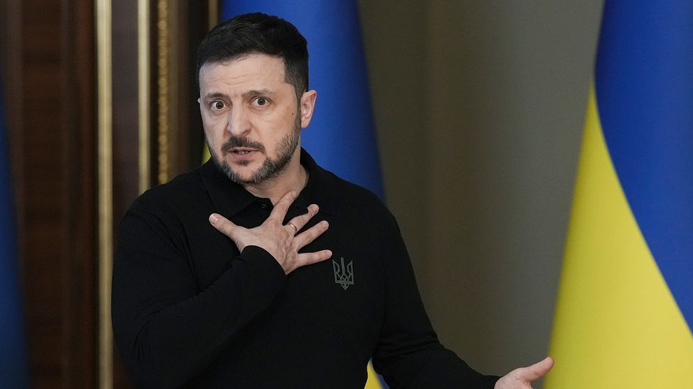 Volodymyr Zelenskyj håller ett tal framför ukrainska flaggor.